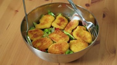 Tahta bir masada metal bir kasede servis edilen gevrek nuggetlarla kaplı taze bir salatanın videosu.