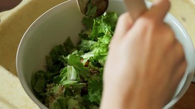 Yavaş çekimde taze bir salatanın ahşap bir kaşık kullanılarak nazikçe karıştırılıp fırlatıldığını gösteren bir video.