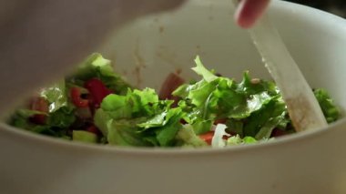 Slow motion video of a fresh salad being gently mixed and tossed using a wooden spoon