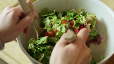 Yavaş çekimde taze bir salatanın ahşap bir kaşık kullanılarak nazikçe karıştırılıp fırlatıldığını gösteren bir video.