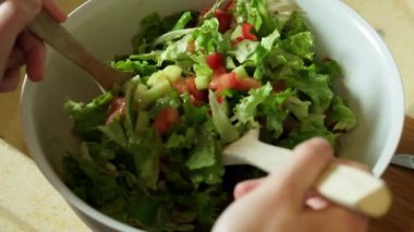 Yavaş çekimde taze bir salatanın ahşap bir kaşık kullanılarak nazikçe karıştırılıp fırlatıldığını gösteren bir video.
