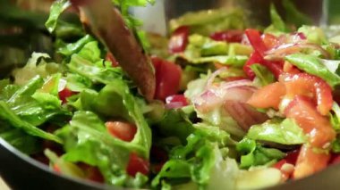 Yavaş çekimde taze bir salatanın ahşap bir kaşık kullanılarak nazikçe karıştırılıp fırlatıldığını gösteren bir video.