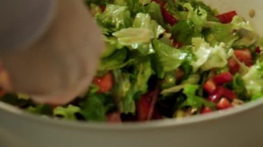 Yavaş çekimde taze bir salatanın ahşap bir kaşık kullanılarak nazikçe karıştırılıp fırlatıldığını gösteren bir video.