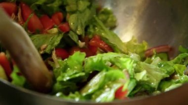 Yavaş çekimde taze bir salatanın ahşap bir kaşık kullanılarak nazikçe karıştırılıp fırlatıldığını gösteren bir video.