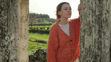 El yapımı turuncu hırka giyen genç bir kadın Hierapolis, Pamukkale 'deki antik harabelerin önünde zarifçe poz veriyor ve hareket ediyor..