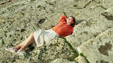 Hierapolis Amfitiyatrosunun antik basamaklarında el yapımı turuncu hırka giyen genç bir kadın video için poz veriyor..