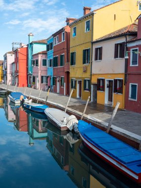 Vibrant row of brightly painted houses along a tranquil canal with moored boats and mirror-like reflections, evoking Mediterranean charm, travel and postcard-perfect scenery. Burano, Veneto, Italy.