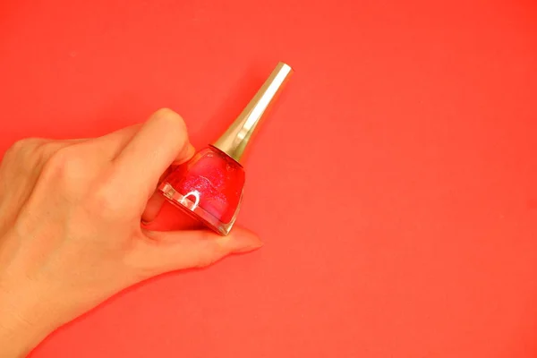 Nail polish in hand on a red background. Manicure. Comsmetics.
