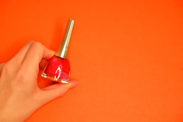 Nail polish in hand on an orange background. Manicure. Cosmetics.