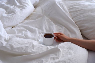 Yatakta kahvaltı. Beyaz çarşaflar. Kızın elinde bir kupa kahve var..