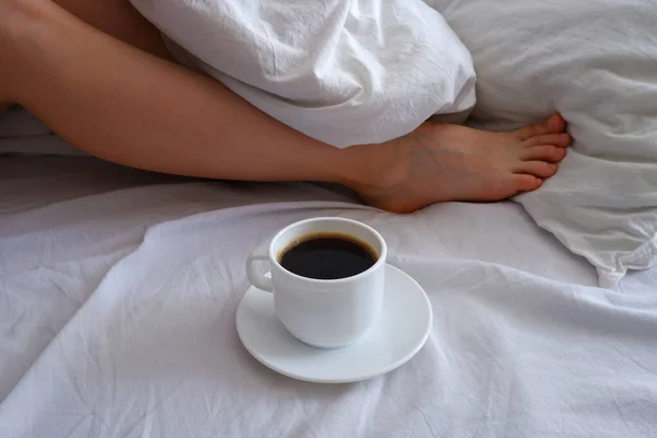 The girl is drinking coffee in bed. A cup of black coffee in a white bed. Breakfast in bed. Interior.