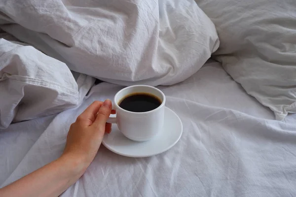 The girl is drinking coffee in bed. A cup of black coffee in a white bed. Breakfast in bed. Interior.