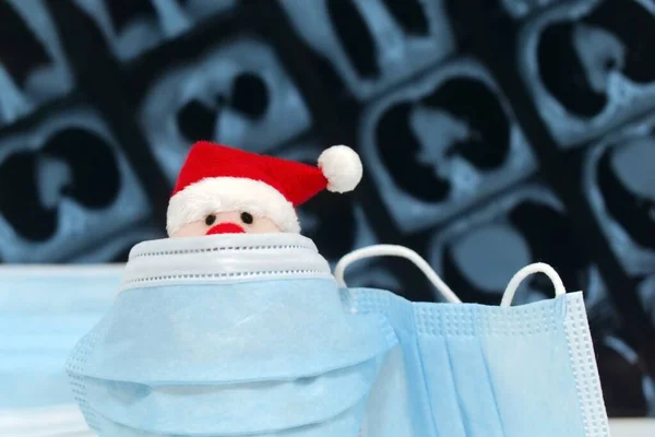 Bulanık arka plan röntgeninde antivirüs koruyucu tıbbi maskenin arkasına saklanan komik Noel Baba oyuncağı.