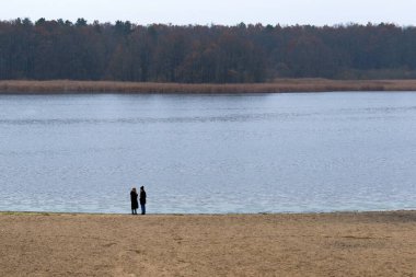Nehrin kumlu kıyısında, diğer taraftaki sonbahar ormanının bulanık arka planında tanınmayan iki kız.