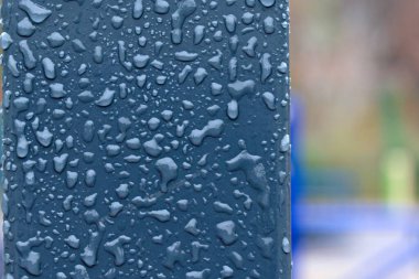 Gri metal paneldeki donmuş yağmur damlaları sağda bulanık arkaplan ile kapanır