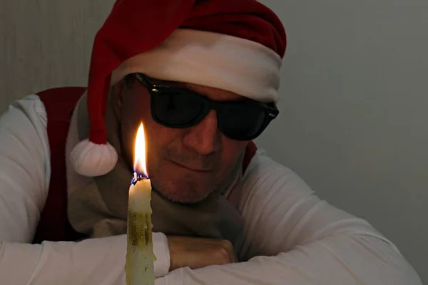 黒い眼鏡とクリスマスキャップの男の背景のぼやけた背景に明るい燃焼火のクローズアップキャンドル — ストック写真