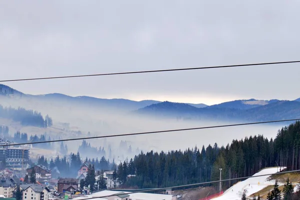 スキーリフトのロープを通って霧の中のスキータウンの谷まで眺め — ストック写真