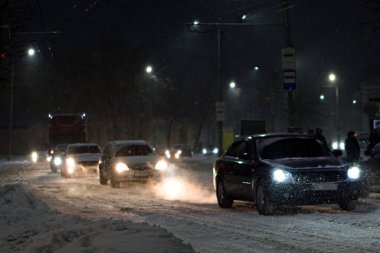 Akşamları yoğun kar yağışı sırasında şehir trafiği. Karlı bir caddede bulanık hareket halinde, farları yanan arabalar.