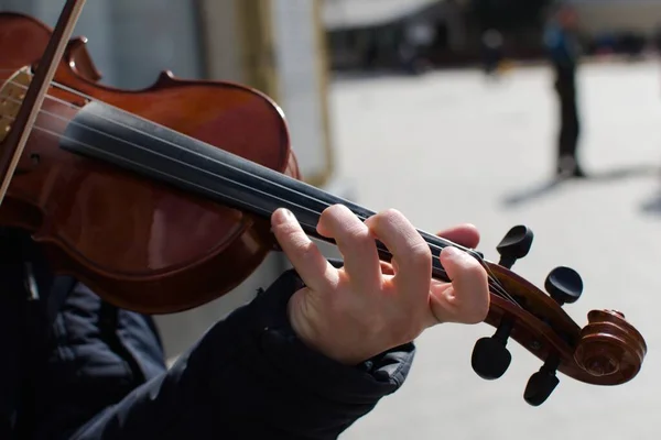 fingers of street violinist on blurred background of violin and sunny street