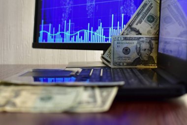 Bilgisayar ekranının bulanık arka planında 20 dolarlık banknotlar ve hisse senedi grafiği. Bulanık arkaplan