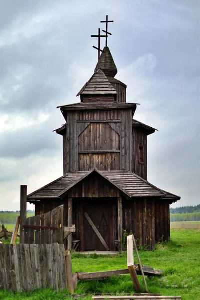 Wooden Orthodox church against background of gloomy sky and green grass