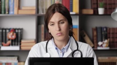 Bilgisayardaki yorgun doktor acı ve rahatsızlık hissediyor. Dizüstü bilgisayarda çalışan, klavyede yazan konsantre kadın doktor ara veriyor ve parmaklarını ve boynunu yoğuruyor.