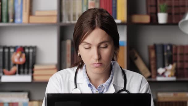 Втомлений сонний лікар за комп'ютером. Виснажена жінка-лікар працює на ноутбуці, друкуючи на клавіатурі в офісі і засинає на робочому місці, її голова падає на її груди і очі близько — стокове відео