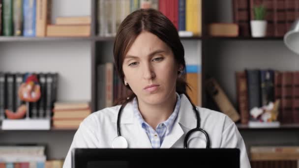 El médico cansado al ordenador experimenta el dolor y la incomodidad. La doctora concentrada en la oficina que trabaja en el ordenador portátil que teclea en el teclado toma descanso y amasar los dedos y el cuello — Vídeo de stock