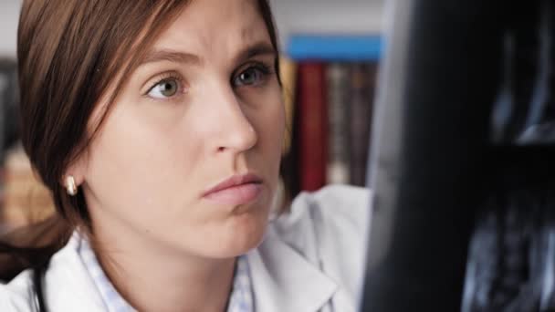 Doctorul se uită la radiografie sau RMN. Închiderea concentrată a feței atractive medic femeie în haină albă, ea se uită îndeaproape la RMN sau la scanarea cu raze X — Videoclip de stoc