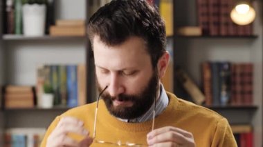 Yakışıklı sakallı bir adamın portresi. Gözlüklerini siliyor ve takıyor. Sonra da gülümseyerek kameraya bakıyor. Yakın plan.