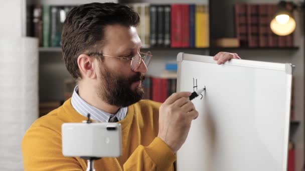 Nätutbildning och distansundervisning. Man kemi lärare talar och tittar in telefonkamera och skriver formel fosforsyra på whiteboard och förklarar detta för sin samtalspartner — Stockvideo