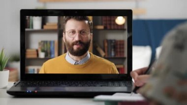 Uzaktan öğrenme, eğitim videosu, online toplantı, video görüşmesi, Webinar konsepti. Kadın eli dizüstü bilgisayarda notlar alır. Gözlüklü adam duygusal olarak kameraya konuşur.
