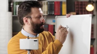 Çevrimiçi eğitim ve uzaktan öğrenme kavramı. Adam İngilizce öğretmeni konuşuyor ve kameraya bakıyor ve manyetik işaret tahtasına İngilizce kelimeler yazıyor. Müfettişine bir şey anlatıyor.