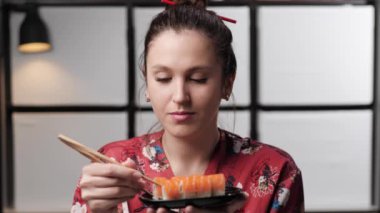 Suşi yiyen bir kadın. Asya tarzı kırmızı elbiseli çekici, mutlu bir kadın siyah porselen tabaktan suşi yiyor, yemekten hoşlanıyor. Yavaş çekim