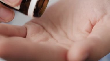 İki büyük, berrak kehribar oval hap kapsülü ilaç şişesinden avuç içine düşer. Yakın çekim, ön görüntü, merkez kompozisyon