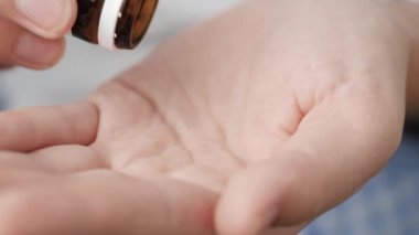 İki büyük beyaz-mavi silindirik kapsül hapı ilaç şişesinden avuç içine düşer. Yakın çekim, ön görüntü, merkez kompozisyon
