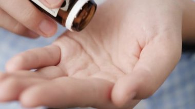 İki büyük beyaz hap oval elmas şekilli uzamış şekiller hap şişesinden avuç içine düşer. Yakın çekim, ön görüntü, merkez kompozisyon