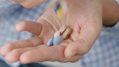 Bir avuç dolusu hap ve çeşitli şekil ve renklerden oluşan kapsüller diğer elden avuç içine düşer. Yakın çekim, ön görüntü, merkez kompozisyon