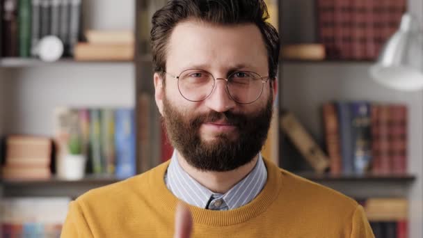 Hombre pulgar hacia arriba. Hombre barbudo sonriente positivo en gafas en la oficina o habitación del apartamento mirando a la cámara y muestra su pulgar hacia arriba. Primer plano y cámara lenta — Vídeos de Stock