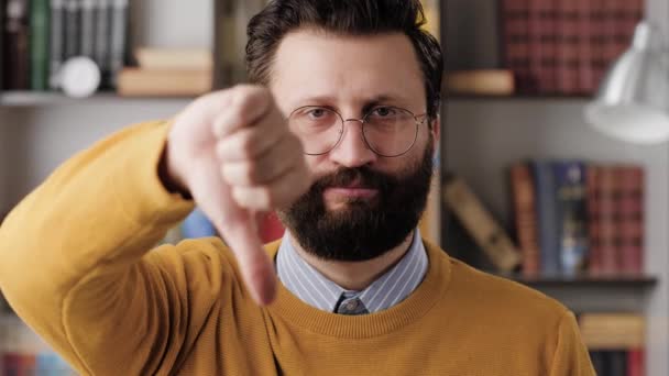 Hombre pulgares hacia abajo. Serios hombre barbudo disgustado con gafas en la oficina o habitación del apartamento mirando a la cámara y muestra su mano con el pulgar hacia abajo. Primer plano y cámara lenta — Vídeos de Stock