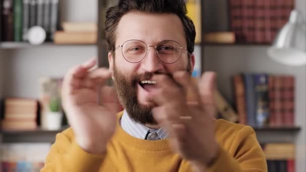 Hombre aplausos. Hombre barbudo sonriente y riéndose positivamente en gafas en la oficina o en la habitación del apartamento mirando a la cámara y aplaudiendo alegremente sus palmas. Primer plano y cámara lenta — Vídeo de stock