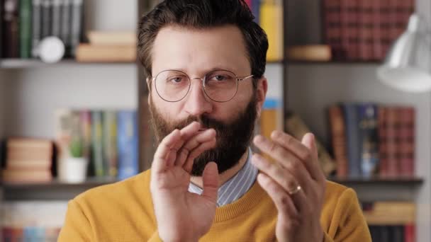 Un aplauso sarcástico. Oscuro hombre barbudo escéptico en gafas en la oficina o habitación del apartamento mirando a la cámara y a regañadientes aplaude sus palmas para crear falsos aplausos. Primer plano y cámara lenta — Vídeo de stock