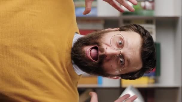 Man is scared, terrified. Vertical video of frightened bearded man in glasses in office or room in apartment with suddenly throws his hands up and looking at camera, he is very scared. Close-up — Vídeo de Stock