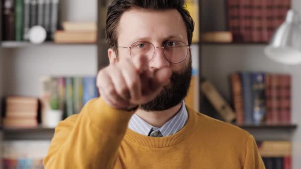 Man beckons with his finger. Serious frowning bearded man with glasses in office or apartment room looking at camera and points his fingers, gesturing to him. Close-up and slow motion — Stockvideo