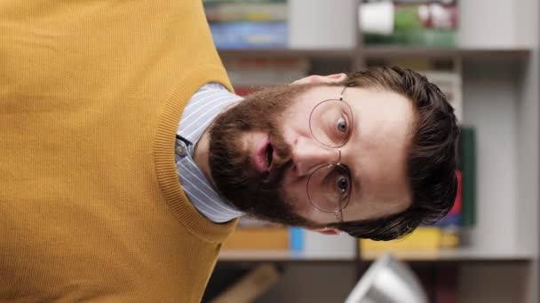 Shh, man secret finger. Vertical video of suspicious bearded man in glasses in office or apartment room looking at camera and brings his index finger to his mouth lips and she say shhh. Close-up — Stockvideo