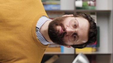 Man nods in agreement. Vertical video of positive bearded man in glasses in office or apartment romm looking at camera and nods his head positively, signaling YES or HELLO. Close-up and slow motion