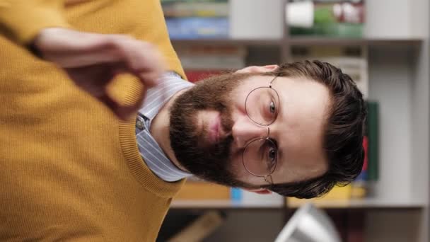Függőleges videó pozitív mosolygós szakállas férfiról szemüvegben az irodában vagy a lakosztályban a kamerába néz, és az ujjával mutatja az OK gesztust. Közelkép és lassított felvétel — Stock videók