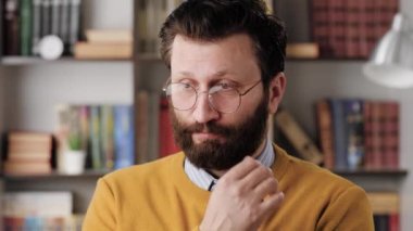 Man is embarrassed, shy. Slightly confused bearded man in glasses in office or apartment room shyly looks away from camera, looks embarrassed. Close-up and slow motion