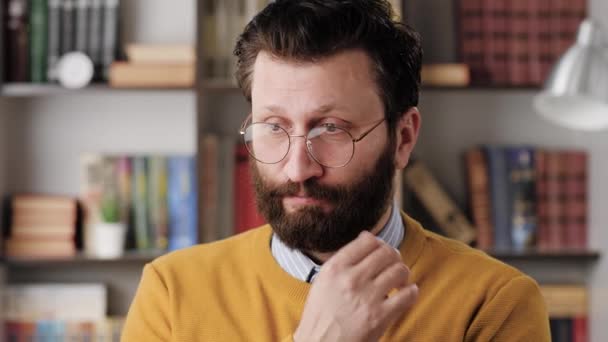 Man is embarrassed, shy. Slightly confused bearded man in glasses in office or apartment room shyly looks away from camera, looks embarrassed. Close-up and slow motion — Stock video