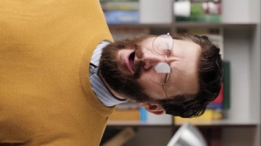 Man yawns. Vertical video of tired sad bearded man in glasses in office or apartment room yawns for long time, he is bored or wants to sleep. Close up and slow motion